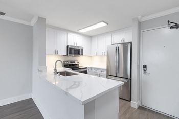 a white kitchen with stainless steel appliances and a white counter top at Nobel Court, San Diego, CA